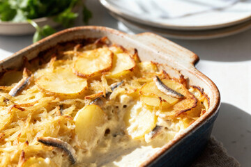 Janssons frestelse, creamy Swedish potato and anchovy casserole baked golden, served in rustic ceramic dish, bright Scandinavian kitchen atmosphere