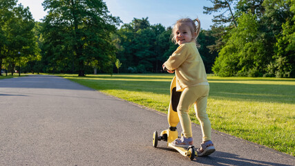 Scooter child. Girl riding scooter toddler. Yellow outdoor activity park road.
