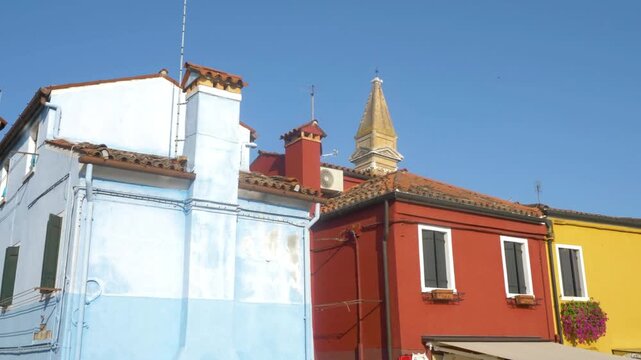 Colorful buildings line a street in burano, italy, under a clear blue sky