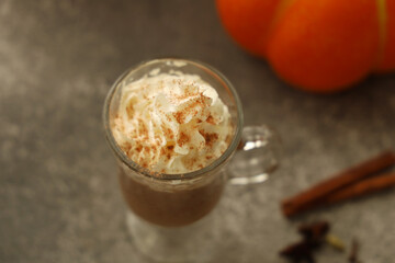 Warm spiced drink topped with whipped cream served in a glass with festive autumn decorations