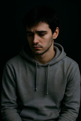 sad brunette boy in gray sweatshirt. realistic photo of grief, depression, nervousness, tragic