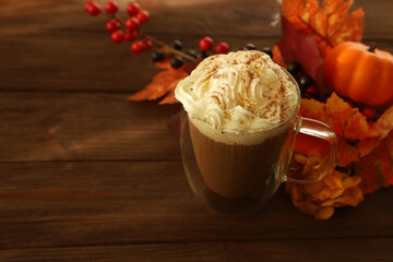 Warm coffee drink topped with cream and spices near autumn leaves and pumpkins