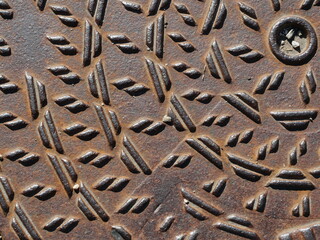 Rusty manhole cover with geometric metal pattern. Detailed close-up