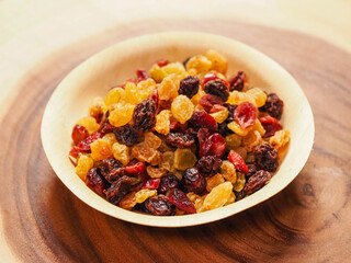 A bowl of dried fruit with yellow and red raisins, cranberries. The bowl is on a wooden table. Natural high sugar and glucose content. Popular snack.