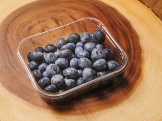 A plastic tray of blueberries sits on a wooden table. The tray is clear and filled with fresh organic fruits ready for consumption. Healthy diet concept. Natural product.