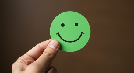 A hand holding a green smiley face sticker against a brown background.