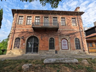 Facade of Varna History Museum, a burgundy historic building with iron grilles, arched windows, terrace, and ivy-covered walls.