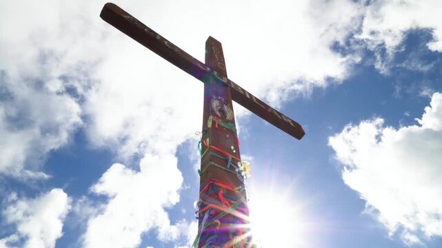 A wooden cross stands tall against a backdrop of blue sky and white clouds