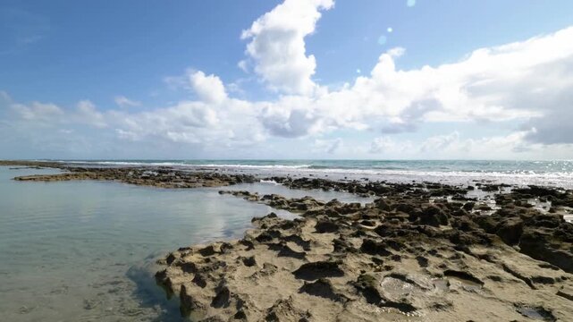 Low angle view of rocky beach and calm ocean under a cloudy blue sky