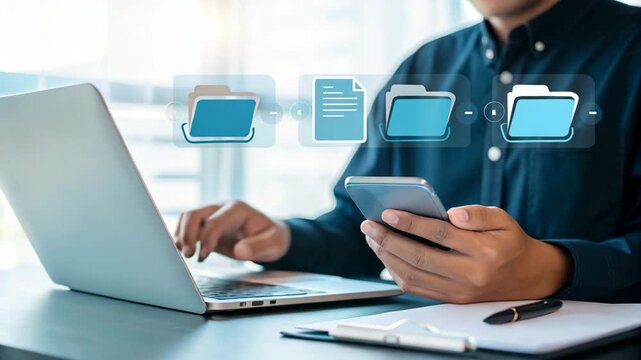 Person using laptop and holding smartphone with file transfer graphic overlay on desk at office area