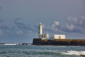 Beautiful white lighthouse on the coast of the sea, with clouds in the background