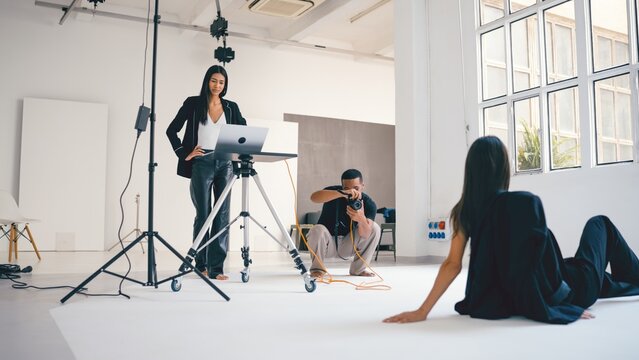 Photographer taking photos of model while art director supervising photoshoot in studio - Powered by Adobe