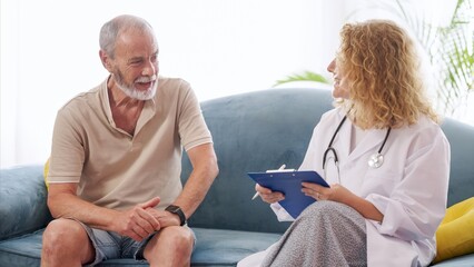 Female doctor visiting senior man at home taking notes on clipboard