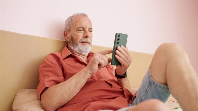 Senior man relaxing on bed using smartphone browsing internet