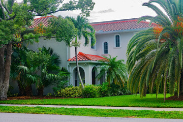 Sunlight filters through palm fronds in a peaceful Naples neighborhood. Stylish home blends tropical landscaping with Mediterranean charm.