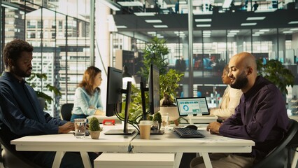 Employee editing documents on desktop computer at office desk, updating reports and files. Worker analyzing data charts on computer screen at desk, interpreting statistical information, camera B