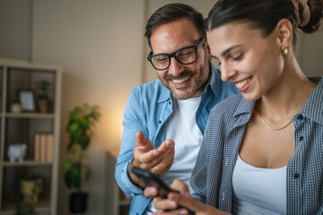 Happy couple enjoying smart phone together at home