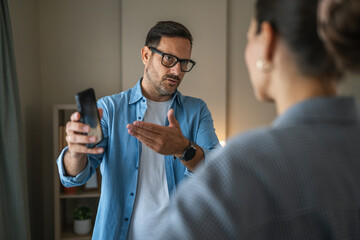 Man showing smart phone to woman, having conflict