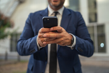 Businessman holding mobile phone outdoors, sending message