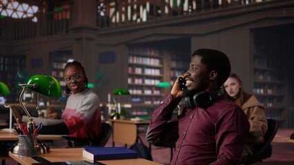 Noisy black guy disturbing pupils at the library by speaking very loud, being rude and answering phone call in the study area. Disruptive annoying man asked to keep silence. Camera B.