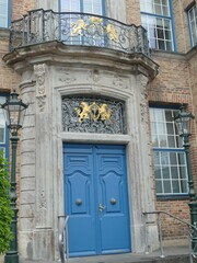 Blue wooden entrance door of an old european building with golden coat of arms, balcony with forged railing and street lamps