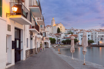 View of the Church of Santa Maria in Cadaques, Spain at sunrise with coastal buildings and calm waterfront