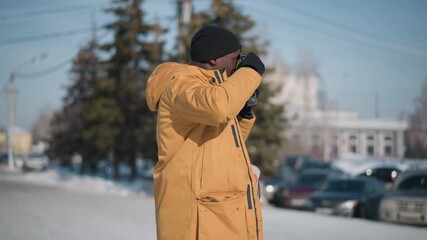 side view of reporter wearing beanie and gloves peering through viewfinder of vintage camera, gloved fingers fine tuning focus dial then pressing shutter against clear blue winter sky bright sunshine