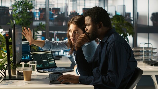 Manager supervising work done by accountant inputting financial figures on PC and checking reports. Supervisor overseeing progress done by man working in office crosschecking data, camera A