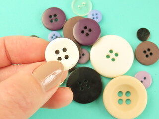Woman hands holding white button. Colorful buttons on green background.	