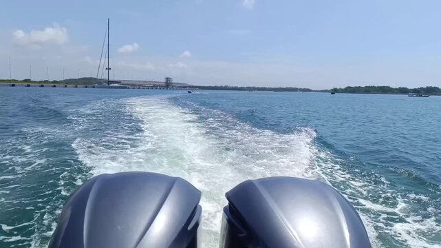 Footage of two outboard motors seen from behind at the stern of a moving boat, creating a trail of waves and water foam.