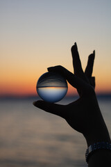 Crystal Ball Held Between Two Fingers, Sunset at Sea, Lensball Resting on Sand and Sunset