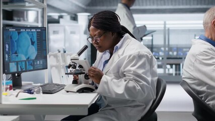 Black scientist examining samples under microscope in a modern laboratory. Research work integrates biotechnology, molecular science and advanced diagnostics to shape medical discovery. Camera B.