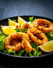 Crispy fried squid rings served on a dark plate with lemon slices and lettuce