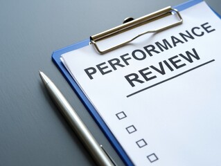 Performance Review document on a blue clipboard with a silver pen on a desk
