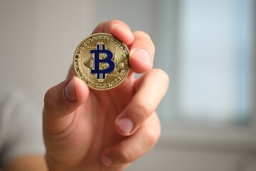 Cryptocurrency. Man holding golden bitcoin against blurred background, closeup. Space for text