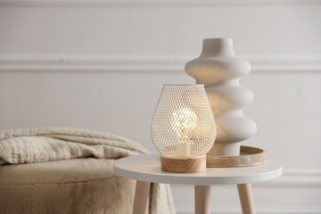 Stylish lamp and vase on white table near pouf indoors