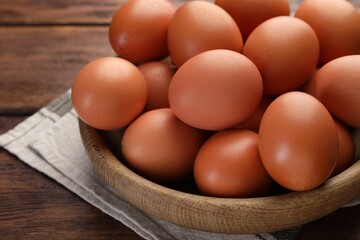Raw chicken eggs in bowl on wooden table, closeup
