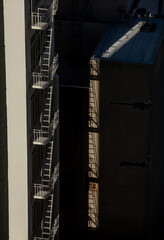 White fire escapes on urban building with dramatic sunlight and shadow contrast