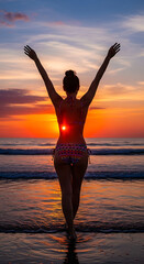 Woman’s back in patterned bikini, arms raised as she walks toward ocean, sun setting behind her