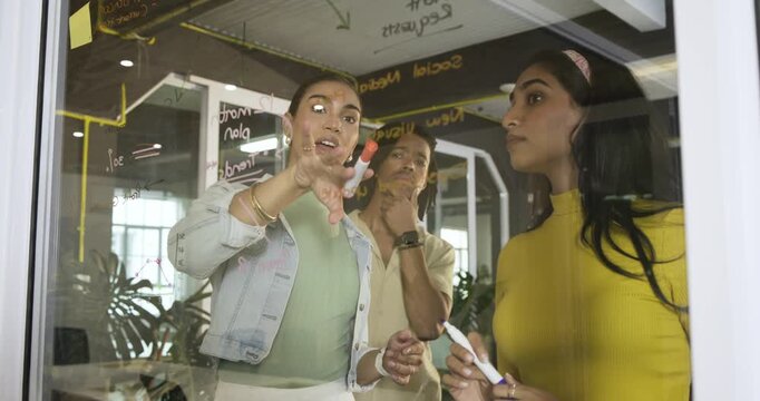 Following brainstorming, Diverse coworkers mapping 12 month plan on glass whiteboard using markers - Powered by Adobe