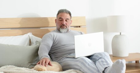 Noticing sleeping cat, man alternating typing on laptop and gently petting cat on bed for calm - Powered by Adobe