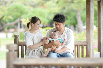 Fototapeta premium A man and a woman are holding a baby on a bench. The baby is wearing a blue shirt