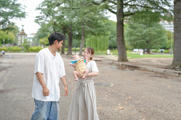 Fototapeta premium A man and a woman are holding a baby in a park. The baby is smiling and the man is wearing a white shirt. The scene is peaceful and happy