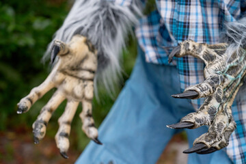 Both werewolf hands reach toward the viewer with sharp black nails and shaggy fur. Plaid shirt and denim jeans finish the creepy outdoor Halloween portrait.