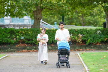 Fototapeta premium A man and woman are walking with a baby in a stroller. The baby is wearing a blue outfit