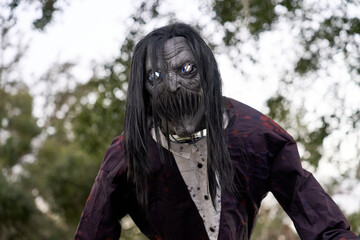 A horrific gray-faced creature with glowing blue eyes leans forward through long hair. Tattered clothing, sharp teeth, and chains suggest a terrifying captive.