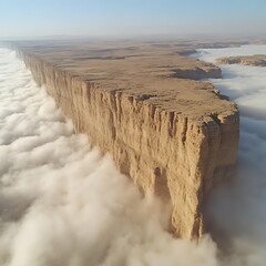 Massive sandstone cliff face rises dramatically above a sea of clouds in a desert landscape.  Vast, arid terrain stretches out below