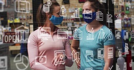 Two adult women wearing masks responding to floating business icons and discussing retail strategy - Powered by Adobe