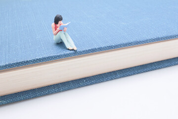 Miniature Woman Reading a Book Sitting on a Blue Hardcover Book
