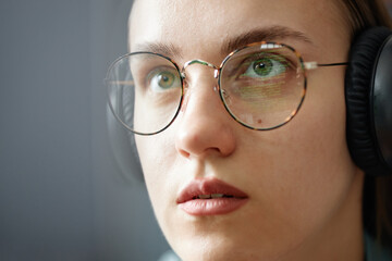 Fototapeta premium Young adult Caucasian woman wearing eyeglasses and headphones looking at computer screen with code reflected in lenses showing focused facial expression